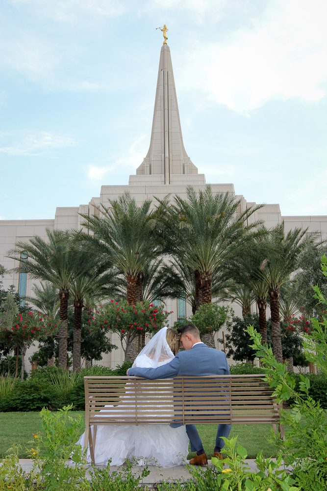 Bride and groom sitting on bench at the Gilbert Arizona Temple with beautiful blue sky with a few clouds behind the temple.