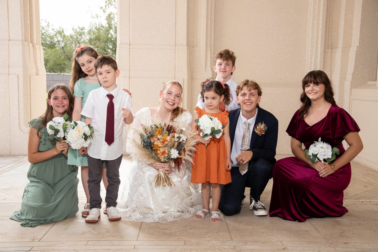 Bride and groom with their bridal party, flower girls, and ring bearers smiling outside the Phoenix Arizona Temple.