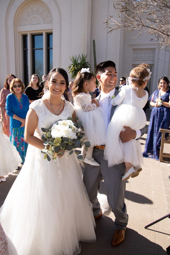 Groom hugs flower girls while the bride watches after the wedding at the Tucson Arizona Temple