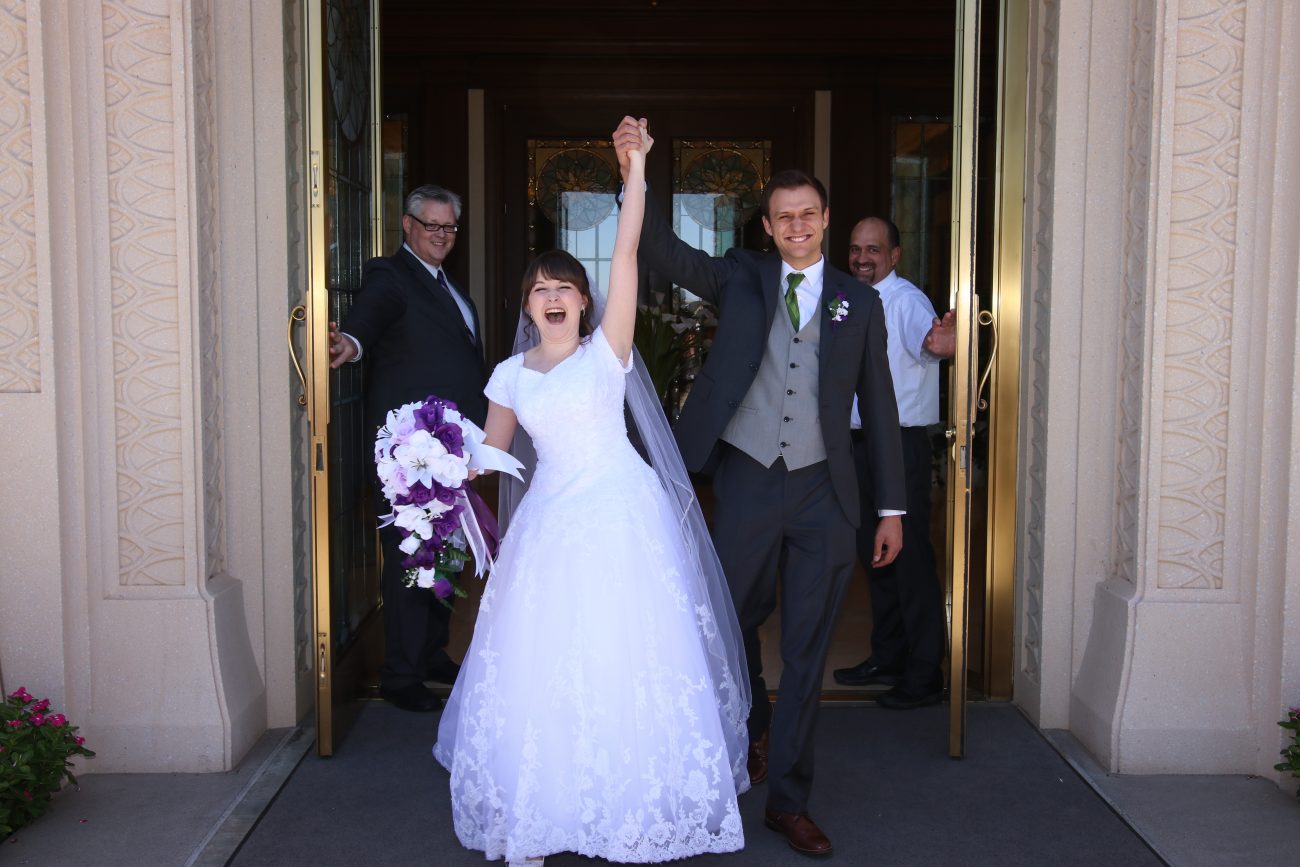 Bride and groom arms outstretched cheering as they exit the Gilbert Arizona Temple after the wedding.