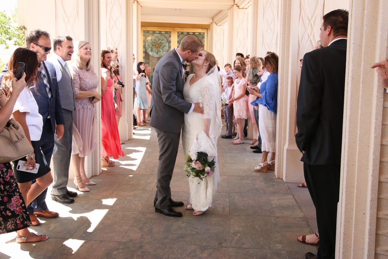 Bride and groom kissing after the wedding at the Gilbert Temple. Friends and family cheering.