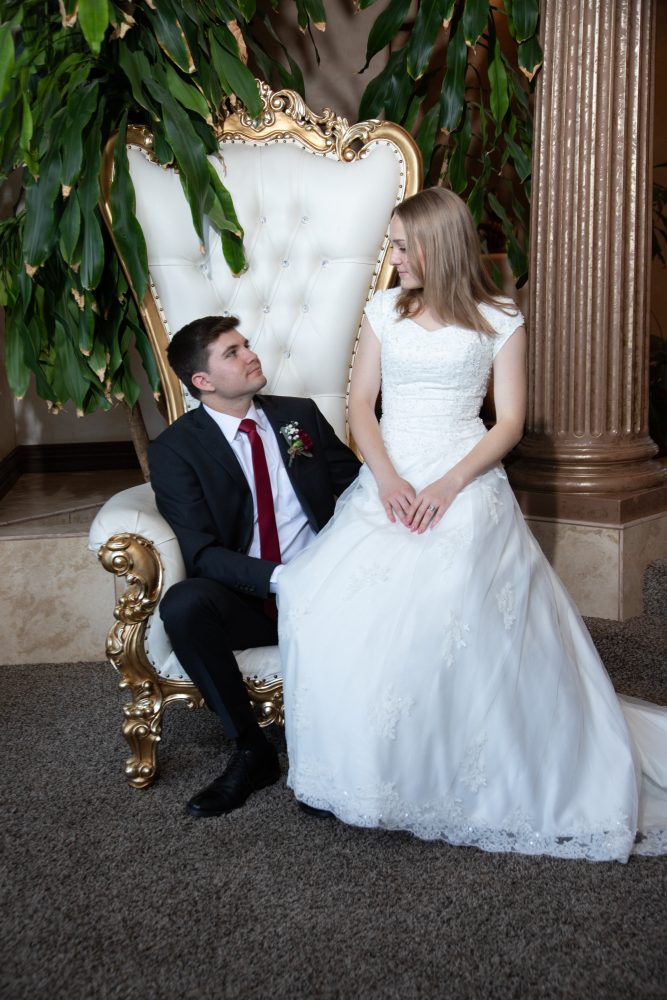 Bride and groom sitting on a very large white chair before the start of their LDS reception.