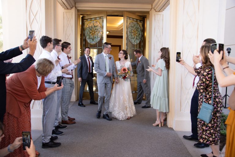 Bride and groom exit the Gilbert temple to cheering friends and family and share a look.